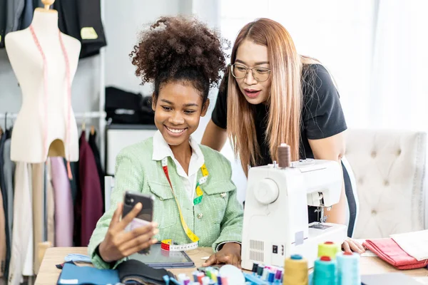 stock image Beautiful two female african american and asian fashion designer using smartphone video call to customer with happiness in tailor shop, Startup small business entrepreneur concept