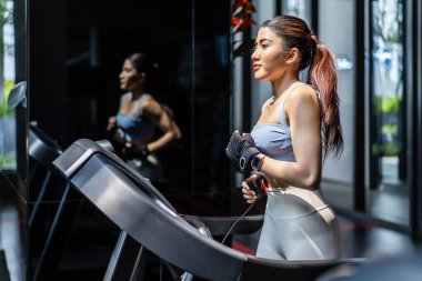 Genç Asyalı bir kız spor salonunda koşu bandında koşuyor, yakın çekim, yan görüş, spor salonunda aktif olarak antrenman yapan kaslı atletler, fitness merkezinde kadın eğitimi. Kardiyo egzersizi yapan kadın.