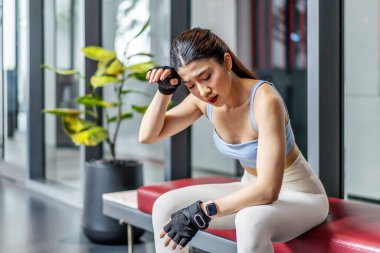 Antrenmandan sonra spor salonundaki genç Asyalı kadının portresi. Beden eğitiminden sonra terli ve nefes darlığı çekiyor. Enerji yakmak ya da spor yapmak için egzersiz yapıyor..