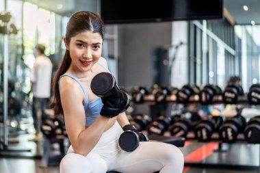 Ağırlık antrenmanı, arka planda ekipmanla ağırlık kaldıran Asyalı genç bir kadın güçlü vücut şekline sahip spor malzemeleri satan bir kız, fotokopi alanı olan Asya yaşam tarzı.