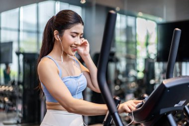 Mükemmel vücut yapısı olan, kulaklık takan Asyalı genç atletik kadın spor salonunda pratik yaparken dinlemek için akıllı telefonlu egzersiz müziği seçiyor.