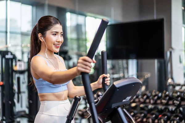 stock image Young asian girl jogging on a treadmill in a gym, Muscular athletes actively training in the gym, Female training at fitness center. Woman exercising cardio workout, exercise lose weight, listen music