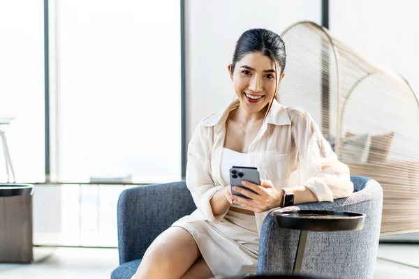 笑顔のアジアの女性は自宅に座ってスマートフォンを使用して保持します ソーシャルメディアを見ています 肖像画 エンターテイメント コミュニケーション 仕事や研究 モバイルアプリ ライフスタイルの概念 ストックフォト