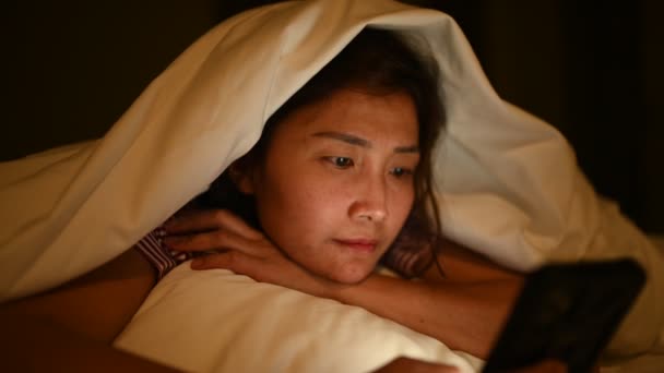 アジアの女性は夜にベッドでスマートフォンでゲームをしています タイ人 ソーシャルメディアを — ストック動画