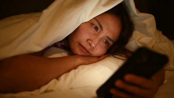 アジアの女性は夜にベッドでスマートフォンでゲームをしています タイ人 ソーシャルメディアを — ストック動画