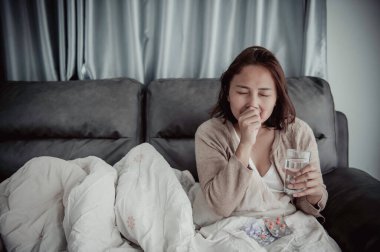 Asyalı hasta kadın kanepede oturur, evde kalır, kadın kendini kötü hisseder, uzanıp dinlenmek ister, yüksek ateş.