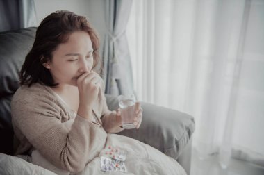 Asyalı hasta kadın kanepede oturur, evde kalır, kadın kendini kötü hisseder, uzanıp dinlenmek ister, yüksek ateş.