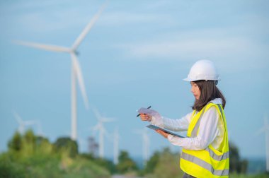 Kadın mühendis, Tayland 'daki dağda rüzgar türbini tarım güç jeneratörü istasyonunda çalışıyor ve raporu tutuyor.