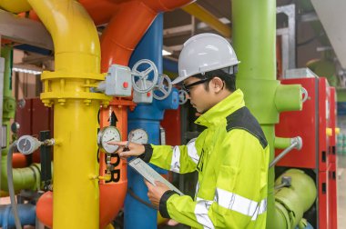 Kazan dairesinde çalışan gözlüklü Asyalı mühendis, ısıtma sistemi ekipmanlarının teknik verilerini kontrol ediyor, Taylandlılar