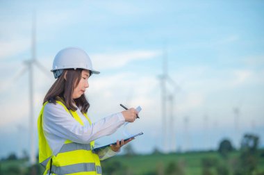 Kadın mühendis, Tayland 'daki dağda rüzgar türbini tarım güç jeneratörü istasyonunda çalışıyor ve raporu tutuyor.