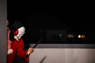 Asyalı yakışıklı adam gece olay yerinde silahlı palyaço maskesi giyiyor, Cadılar Bayramı festivali konsepti, turuncu kıyafetli bir katilin korkunç fotoğrafı, şeytani palyaço avcısı.