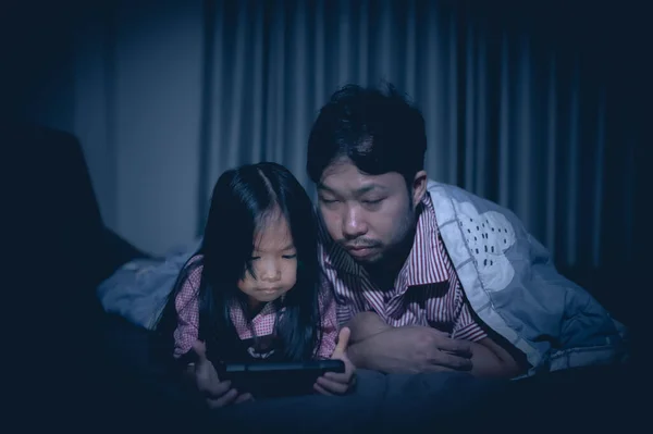 Dad and daughter sleep on the bed in bedroom,Watch cartoon with phone,Father day concept,Single dad,listen tale before sleep