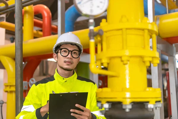 Asian engineer wearing glasses working in the boiler room,maintenance checking technical data of heating system equipment,Thailand people