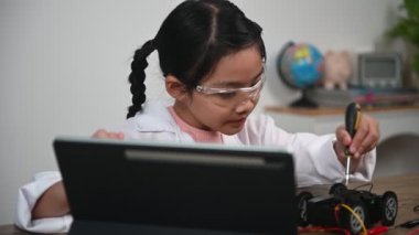 Asian little girl constructing and coding robot at STEM class. Fixing and repair mechanic toy car