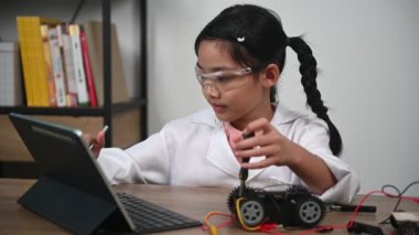 Asian little girl constructing and coding robot at STEM class. Fixing and repair mechanic toy car