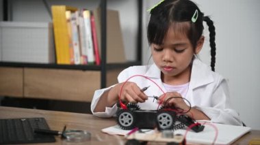 Asian little girl constructing and coding robot at STEM class. Fixing and repair mechanic toy car