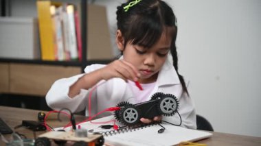 Asian little girl constructing and coding robot at STEM class. Fixing and repair mechanic toy car