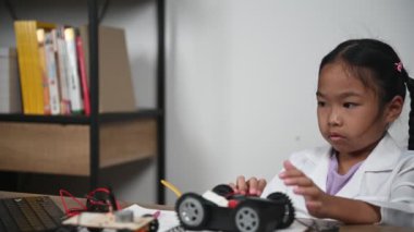 Asian little girl constructing and coding robot at STEM class. Fixing and repair mechanic toy car