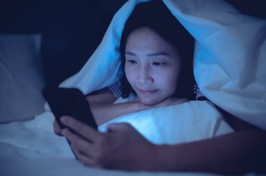 Asyalı kadın gece yatakta akıllı telefonla oyun oynuyor, Taylandlılar, sosyal medya bağımlısı.