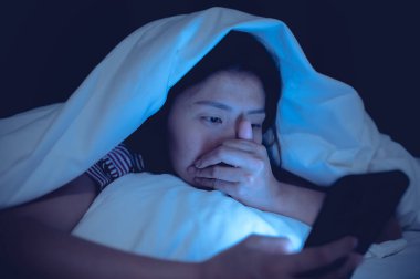 Asyalı kadın gece yatakta akıllı telefonla oyun oynuyor, Taylandlılar, sosyal medya bağımlısı.