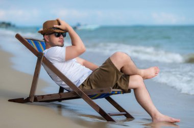 Asyalı bir adam denizin içinde sahilde oturuyor, Yazın dinlenme zamanı