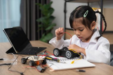 Küçük Asyalı kız STEM sınıfında robot yapıp kodluyor, mekanik oyuncak araba tamir ediyor ve tamir ediyor.