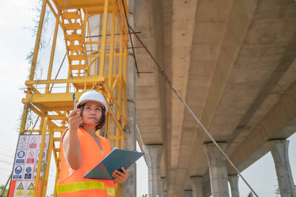 An Asian female engineer works at a motorway bridge construction site,Civil worker inspecting work on crossing construction