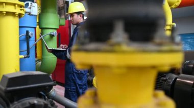 Isıtma tesisinde bakım teknisyeni. Petrokimya işçisi fabrikadaki gaz ve petrol boru hatlarının işletilmesini denetliyor. Mühendis işitme koruyucuyu birçok boruyla aynı odaya koydu.