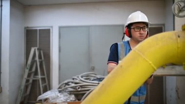 Isıtma tesisinde bakım teknisyeni. Petrokimya işçisi fabrikadaki gaz ve petrol boru hatlarının işletilmesini denetliyor. Mühendis işitme koruyucuyu birçok boruyla aynı odaya koydu.