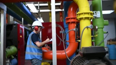 Isıtma tesisinde bakım teknisyeni. Petrokimya işçisi fabrikadaki gaz ve petrol boru hatlarının işletilmesini denetliyor. Mühendis işitme koruyucuyu birçok boruyla aynı odaya koydu.