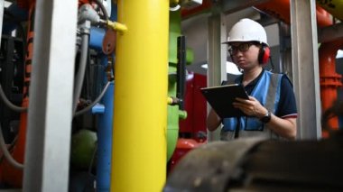 Isıtma tesisinde bakım teknisyeni. Petrokimya işçisi fabrikadaki gaz ve petrol boru hatlarının işletilmesini denetliyor. Mühendis işitme koruyucuyu birçok boruyla aynı odaya koydu.