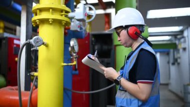 Isıtma tesisinde bakım teknisyeni. Petrokimya işçisi fabrikadaki gaz ve petrol boru hatlarının işletilmesini denetliyor. Mühendis işitme koruyucuyu birçok boruyla aynı odaya koydu.