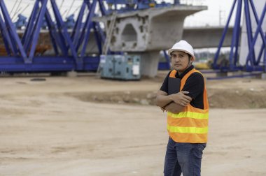 Asyalı mühendislerden oluşan bir grup inşaat alanındaki çalışmalar hakkında konuşuyor, müteahhit ekip binanın tasarımını tartışıyor, üç işçi dışarıda çalışıyor..