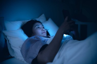 Asyalı kadın gece yatakta akıllı telefonla oyun oynuyor, Taylandlılar, sosyal medya bağımlısı.
