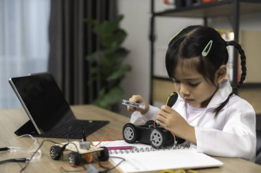 Küçük Asyalı kız STEM sınıfında robot yapıp kodluyor, mekanik oyuncak araba tamir ediyor ve tamir ediyor.