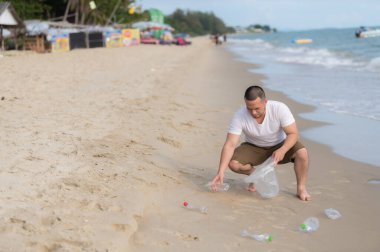 Asyalı adam çöpleri deniz sahilinde tutar, insanlar çöpleri plastik şişelerle saklamaya gönüllü olur.