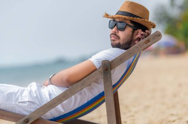 Asyalı bir adam denizin içinde sahilde oturuyor, Yazın dinlenme zamanı