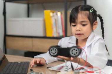 Küçük Asyalı kız STEM sınıfında robot yapıp kodluyor, mekanik oyuncak araba tamir ediyor ve tamir ediyor.