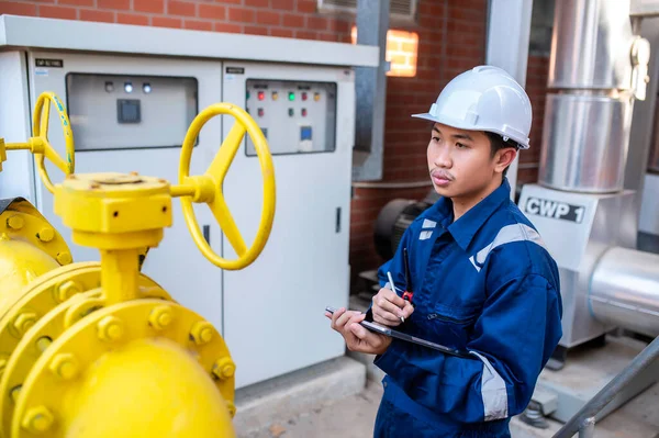 Young engineer working at large factory,Technician in protective uniform and with hardhat  checking temperature in pipes,Read the pressure on the pressure dispenser.