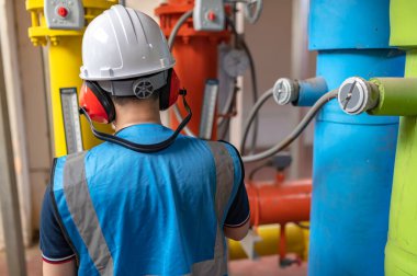 Bir ısıtma tesisinde bakım teknisyeni, Petrokimya işçileri fabrikadaki gaz ve petrol boru hatlarının işleyişini denetliyor, mühendisler işitme koruyucularını birçok boruyla aynı odaya koyuyorlar.