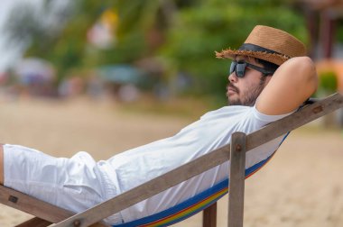 Asyalı bir adam denizin içinde sahilde oturuyor, Yazın dinlenme zamanı