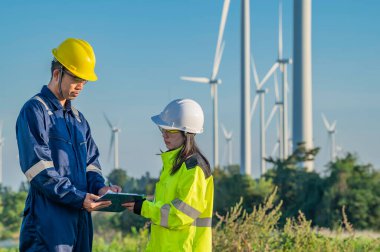 Taylandlı iki mühendis rüzgar türbini çiftliği güç jeneratörü istasyonunda çalışıyor ve raporları tutuyor. Teknisyen erkek ve kadın iş hakkında tartışıyorlar.