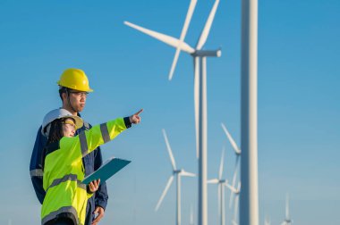 Taylandlı iki mühendis rüzgar türbini çiftliği güç jeneratörü istasyonunda çalışıyor ve raporları tutuyor. Teknisyen erkek ve kadın iş hakkında tartışıyorlar.