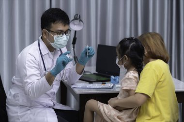 Ebeveynler grip aşısı için kızlarını doktora getirirler, anne çocuğu klinikteki doktora getirir..