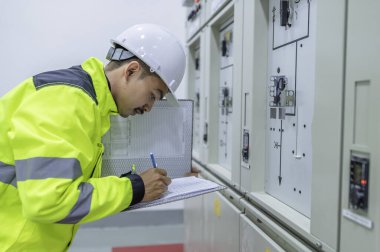 Elektrik mühendisi kontrol odasındaki elektrik dağıtım kabinesinde voltajı kontrol ediyor. Yıllık önleyici bakım, Tayland Elektrikçisi.