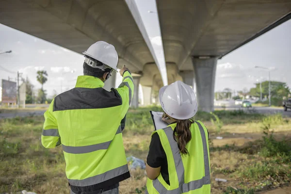 Two engineers discuss about work at the site of large bridge under construction,Management consulting people discussion with engineers about the progress and construction planning of highway
