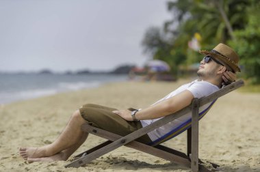 Asyalı bir adam denizin içinde sahilde oturuyor, Yazın dinlenme zamanı