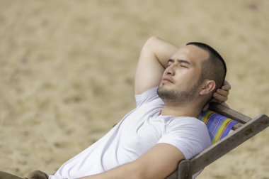 Asyalı bir adam denizin içinde sahilde oturuyor, Yazın dinlenme zamanı