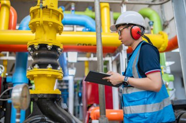 Bir ısıtma tesisinde bakım teknisyeni, Petrokimya işçileri fabrikadaki gaz ve petrol boru hatlarının işleyişini denetliyor, mühendisler işitme koruyucularını birçok boruyla aynı odaya koyuyorlar.