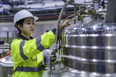 Tayland 'da, ameliyathanede çalışan Asyalı mühendis kask takıyor, özenle ve sabırla çalışıyor, hidrojen tankının valf düzenleyicisini kontrol ediyor..